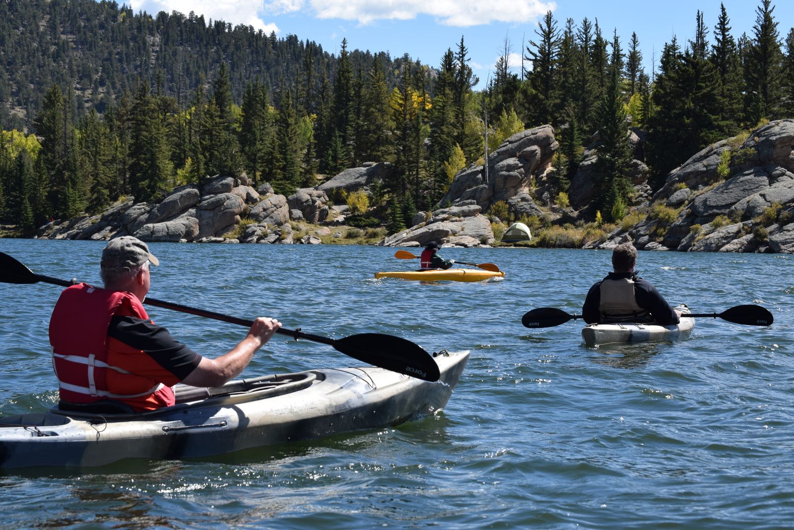 Kayakers paddling across a pine-ringed mountain lake in summer